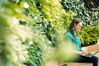 Dame am Computer vor einer grünen Blätterwand, welche für den nachhaltigen Umgang mit Speicherdaten | LEW Green Data Center